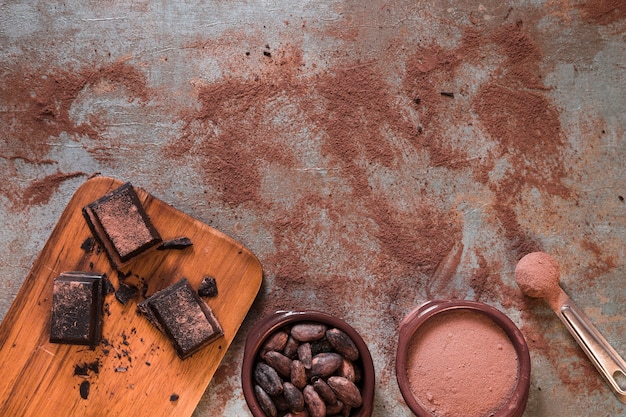 Bowl of cocoa powder and beans with chocolate pieces on chopping board