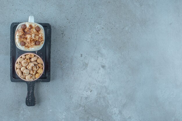 A bowl of cornflakes and a cup of cappuccino on a board , on the blue background.