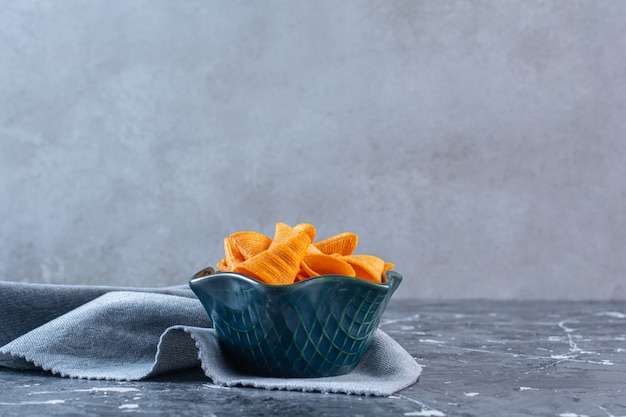 Free photo a bowl of crispy potato chips on a piece of fabric , on the marble surface