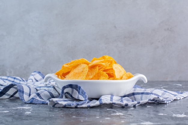 Free photo a bowl of delicious potato chips on a tea towel, on the marble surface