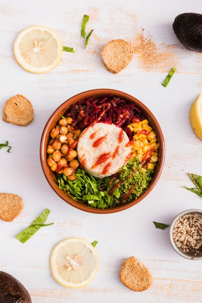 Free photo bowl dish with rice and vegetables surrounded with lemon and bread on white textured backdrop