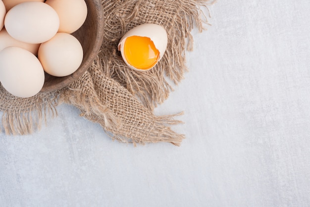 Bowl of eggs next to yolk in a shell on a piece of cloth on marble table.