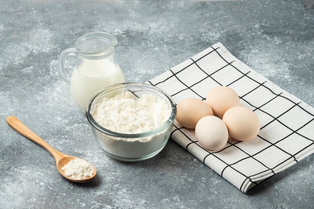 Bowl of flour, eggs and milk on marble.