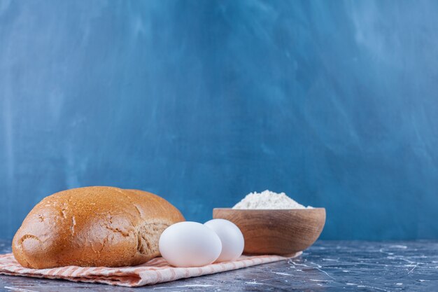 A bowl of flour, lavash and sliced bread on a tea towel, on the blue table.