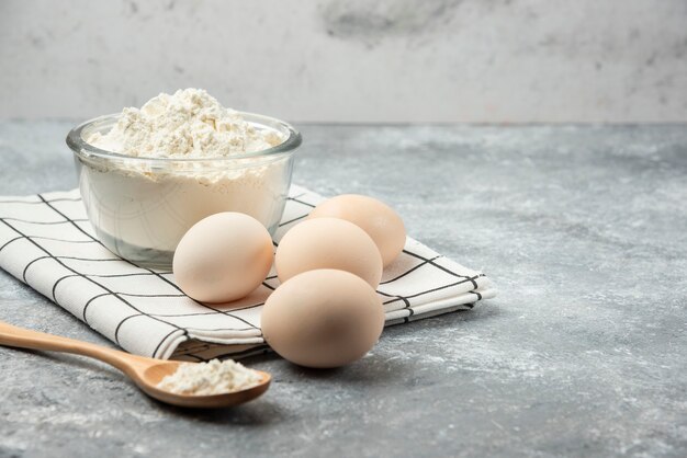 Bowl of flour and raw eggs on tablecloth.