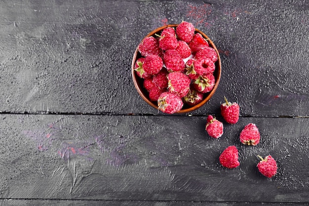 Bowl of fresh red raspberries on dark wooden table. 