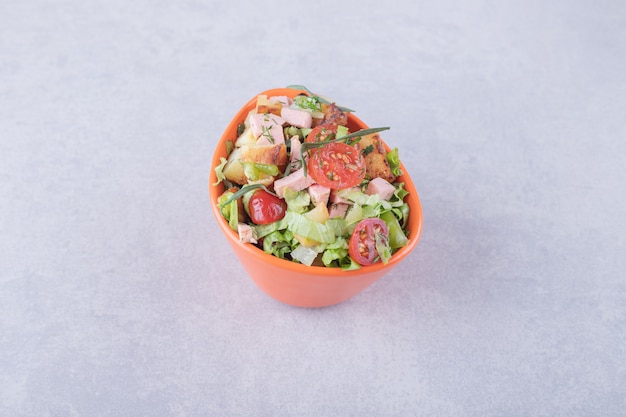 Bowl of fresh salad with sausages on marble background. 