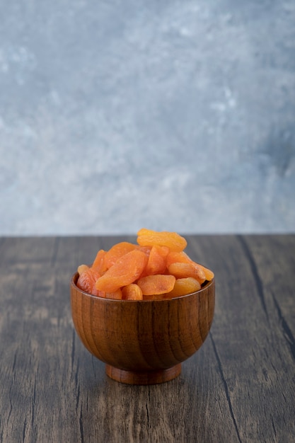 A bowl full of healthy dried apricot fruits on a wooden table .