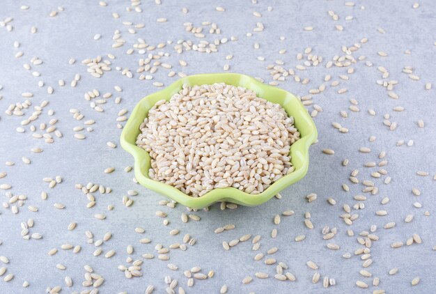 Bowl full of rice in the midst of scattered grains on marble surface