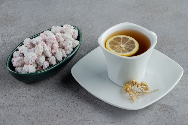 A bowl full of sweet white candies with a glass cup of hot tea on a stone 