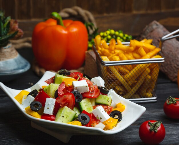 Bowl of greek salad garnished with yellow bell pepper, served with fries