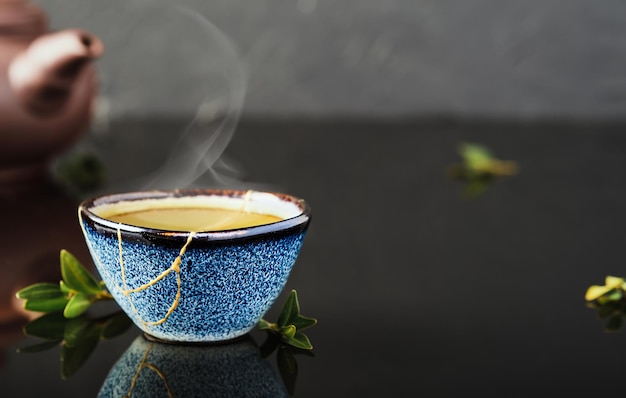 Free photo bowl of green japanese tea, tea leaves lie next the cup. selective focus on the cup. steam rises above the bowl. reclaimed ceramic blue cup, second life of things, recycling or kintsugi