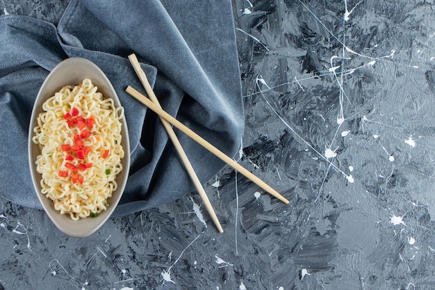 A bowl of noodle next to chopsticks on a pieces of fabric, on the marble background. 