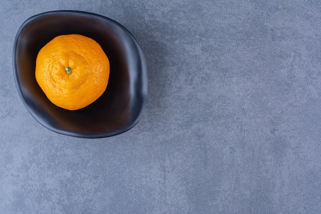 A bowl of oranges, on the dark surface