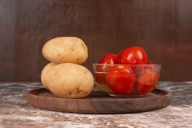 Bowl of pickled tomatoes and boiled potato on wooden plate. 