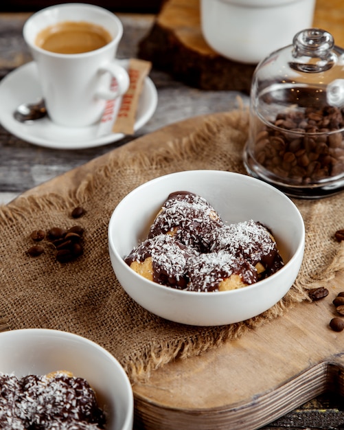 bowl of profiteroles topped with chocolate sauce and coconut sprinkles