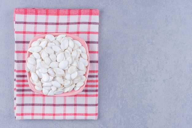 Bowl of pumpkin seed on tea towel on marble.