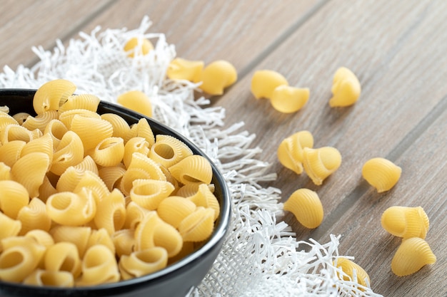 Free photo bowl of raw dry seashell pasta placed on wooden surface