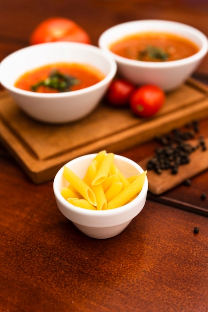 Bowl of raw penne pasta with tomato sauce and black peppercorn on wooden table