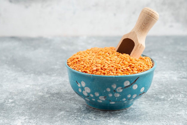 Bowl of raw red lentils on marble table with spoon.