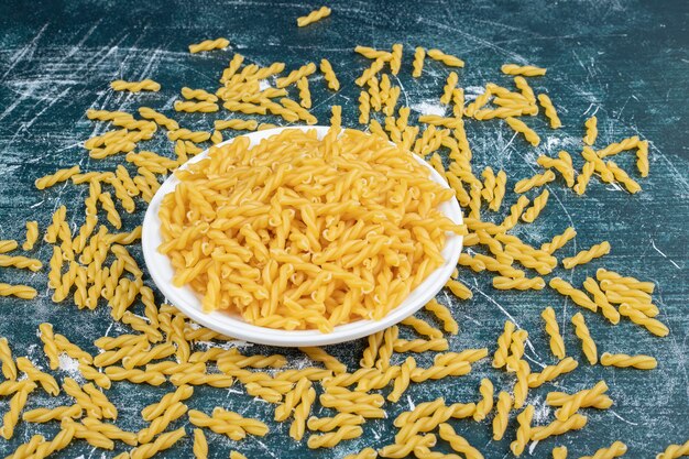 Bowl of raw spiral pasta on blue background. High quality photo