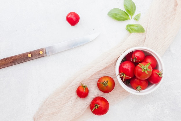 Bowl of red cherry tomatoes with basil leaves; scarf and sharp knife