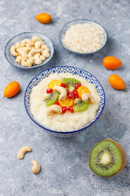 Bowl of rice flakes porridge with kiwi slices, pomegranate seeds, cumquats and cashew nuts, top view