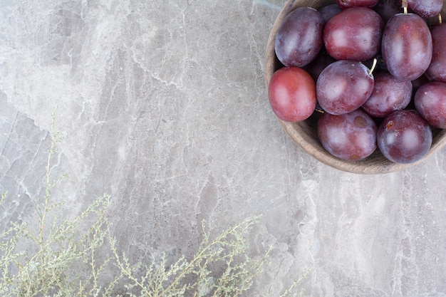 Free photo bowl of ripe plums on stone background.