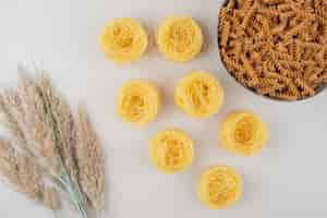 Free photo bowl of spiral pasta and spaghetti nests on white surface