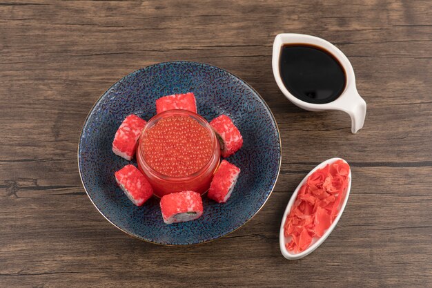 Bowl of sushi rolls and red caviar on wooden table with soy and ginger