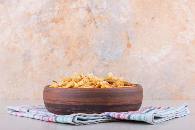 Bowl of tasty crispy crackers with tablecloth on marble background.