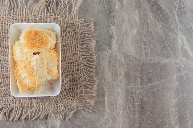 A bowl of Turkish dessert kadayif on a texture on blue.