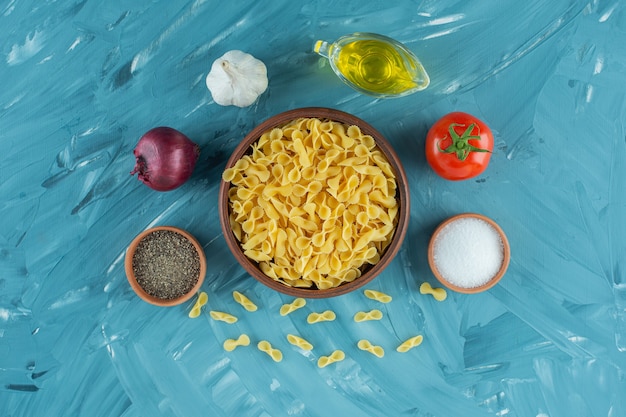 Bowl of uncooked dry macaroni and fresh vegetables on blue background. 