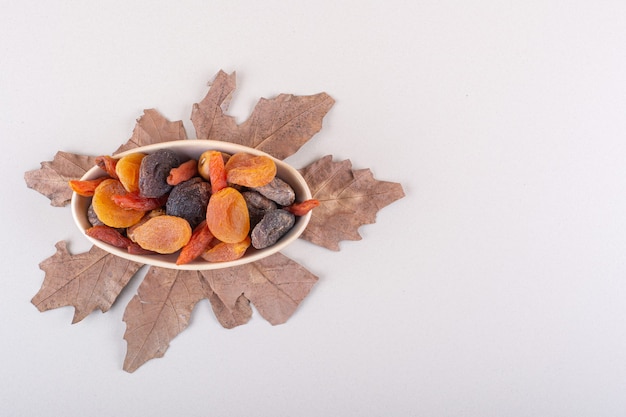 Bowl of various organic fruits with dry leaf on white background. High quality photo