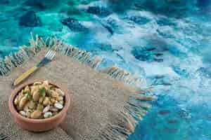 Free photo a bowl of white beans next to fork on a texture , on the blue table.