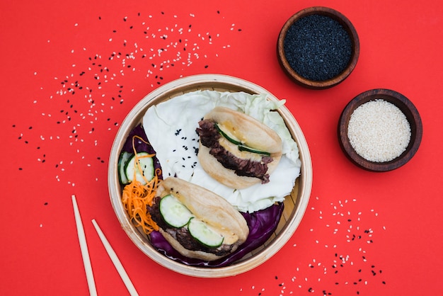 Free Photo bowl of white and black sesame seeds with gua bao in steamer on red backdrop