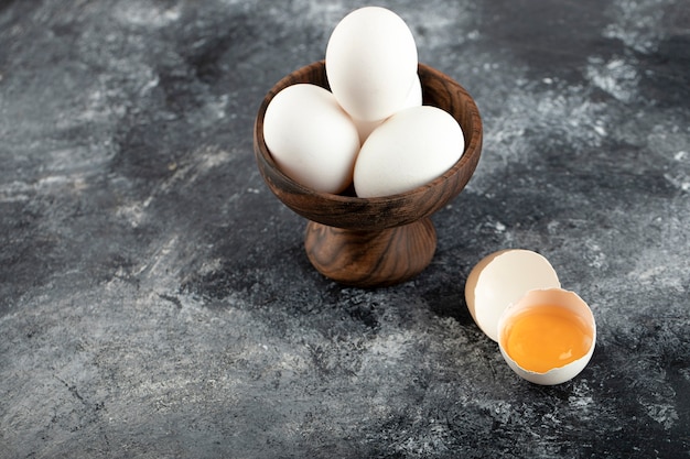 Free photo bowl of white eggs and broken egg on marble surface.