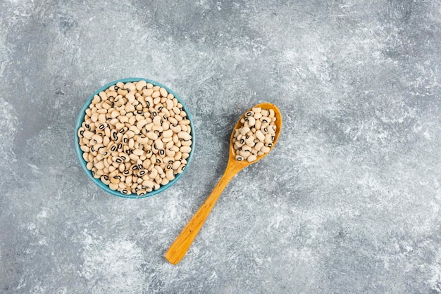 Bowl of white kidney beans with spoon on marble table.