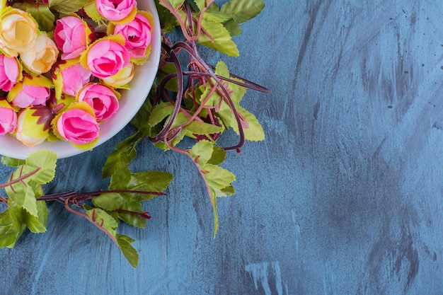 A bowl with artificial colorful roses on blue.