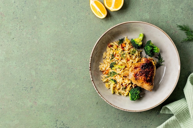 Bowl with chicken pasta orzo with vegetables in Mediterranean style on a green background