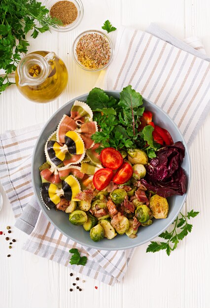 Bowl with Farfalle pasta, Brussels sprouts with bacon and fresh vegetable salad. Flat lay. Top view