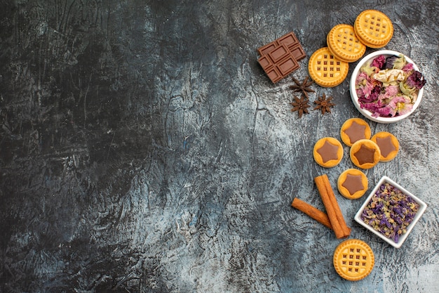 Bowls of dry flowers with cookies and chocolates bars and cinnamons on right side of grey ground