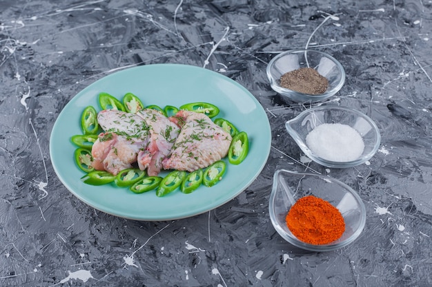 Free Photo bowls full of different spices next to plate with wings and peppers on the blue surface