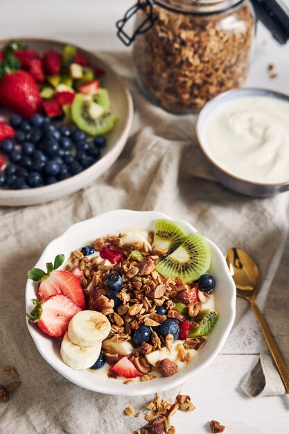 Bowls of granola with yogurt, fruits and berries on a white surface