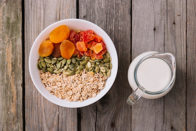 Bowls of muesli, pumpkin seeds and dry fruits in the bowl with milk jug on rustic wooden table