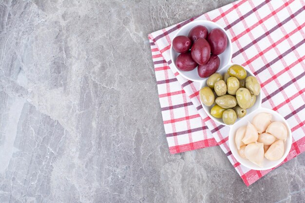 Bowls of pickled plums, olives and garlic on tablecloth.