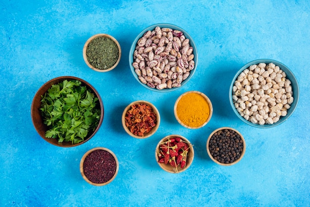 Bowls of raw beans and spices on blue background.