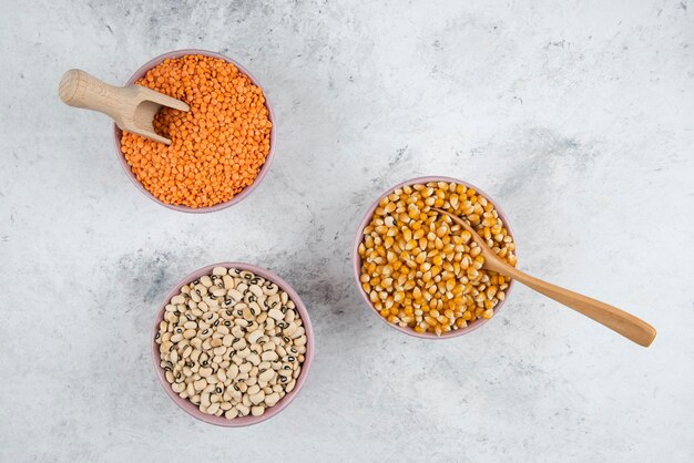 Bowls of raw corns, beans and red lentil on marble surface.