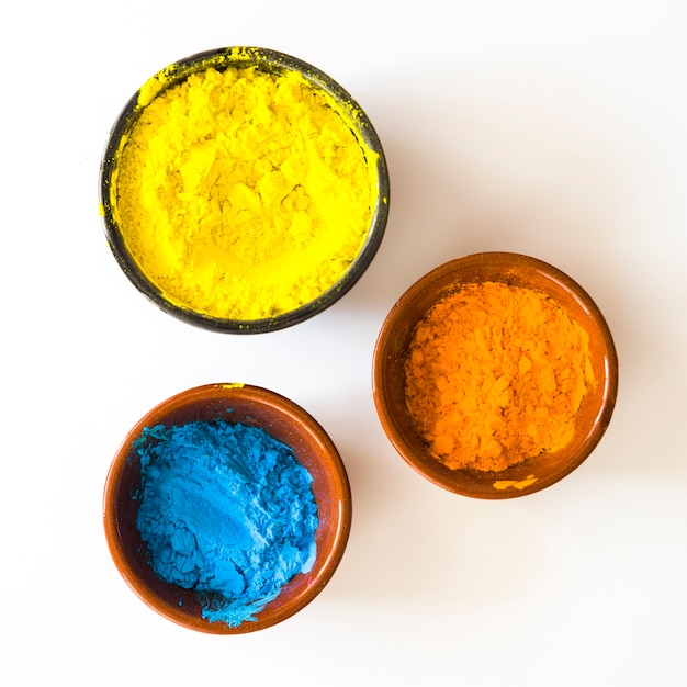 Free photo bowls of yellow; orange and blue color powder isolated on white background