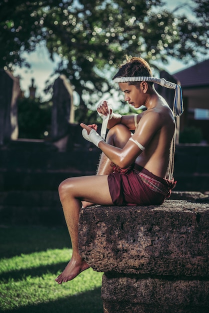 Free photo the boxer sat on the stone, tied the tape around his hand, preparing to fight.